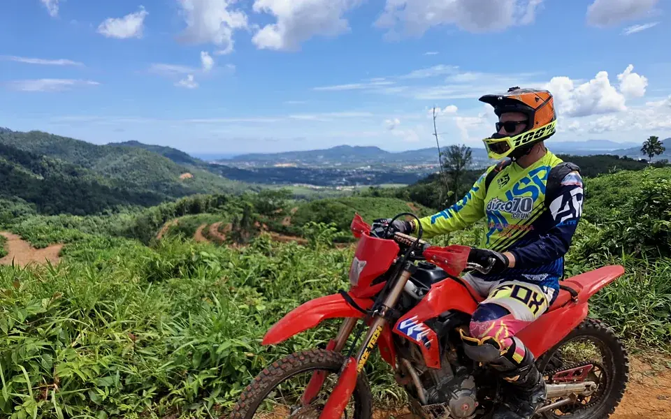 A rider in a helmet, goggles, jersey and gloves on a red Honda, a green valley behind